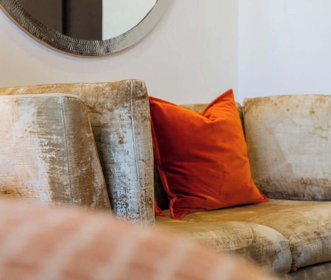 A worn sofa with a single orange cushion against a plain wall.