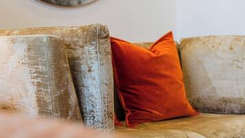 A worn sofa with a single orange cushion against a plain wall.