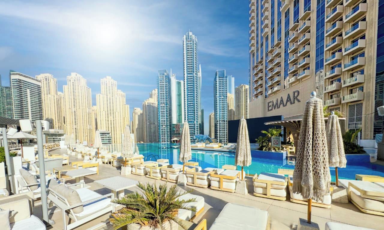 A rooftop pool area with lounge chairs and umbrellas, surrounded by high-rise buildings.