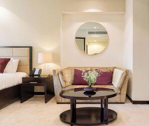 Habitación de hotel con cama, sofá, una mesa redonda con un florero y un espejo en la pared.