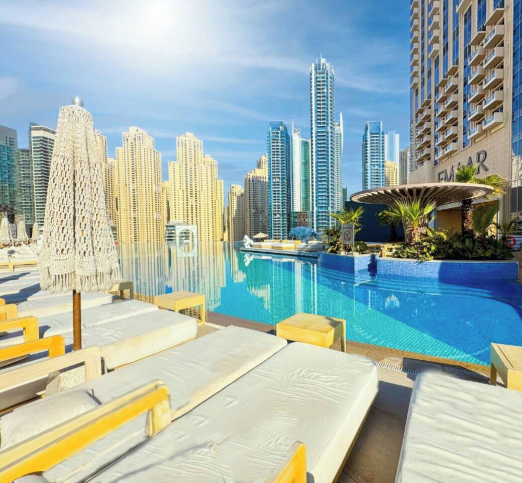 Un área de piscina con sillones de descanso, un elemento acuático y un horizonte urbano al fondo.