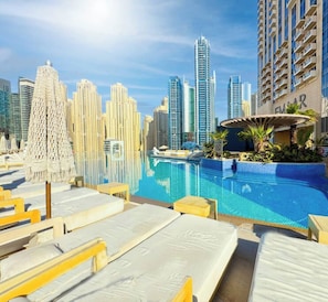 Un área de piscina con sillones de descanso, un elemento acuático y un horizonte urbano al fondo.