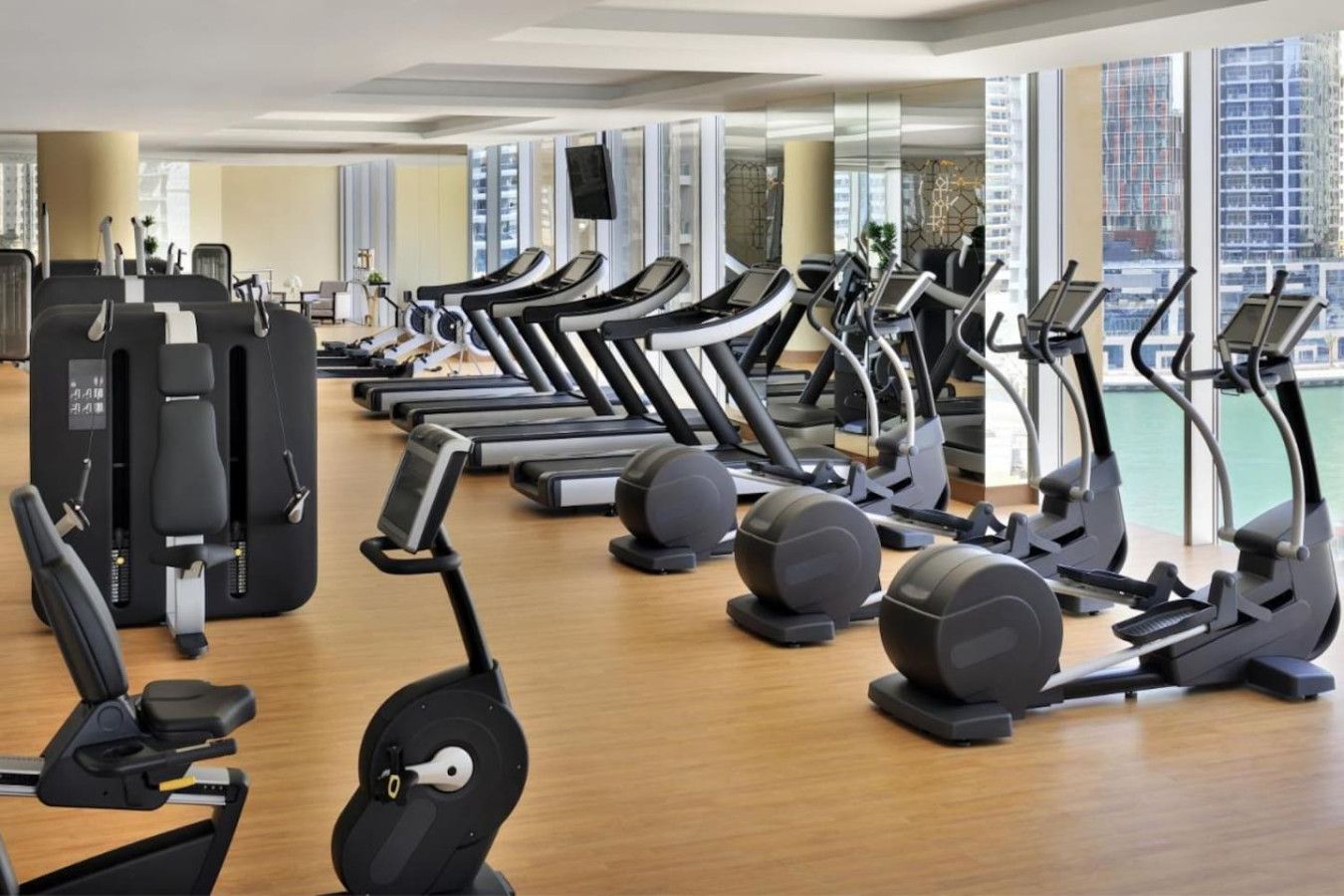 A gym with multiple treadmills, elliptical machines, and weight machines arranged in rows.