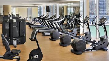 Un gimnasio con varias cintas de correr, elípticas y máquinas de pesas dispuestas en filas.