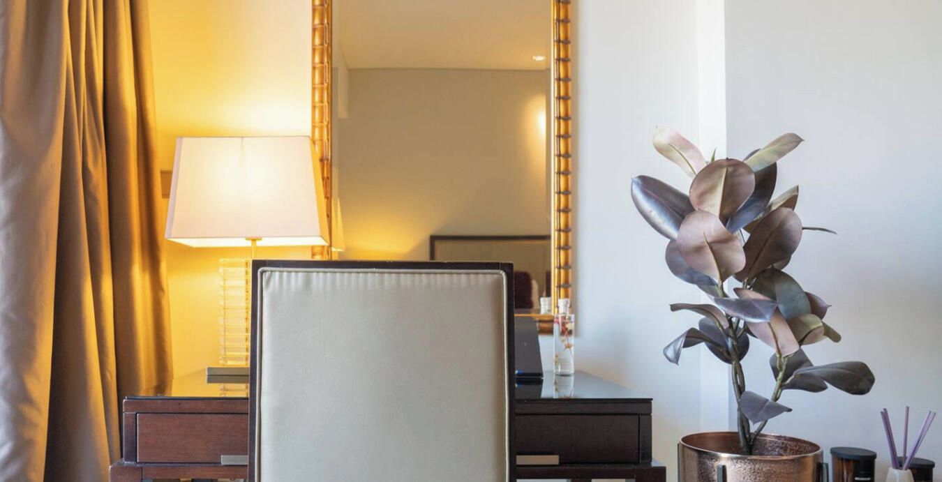 Une chambre d’hôtel avec un lit, une table de chevet, une lampe, un miroir et une plante en pot.