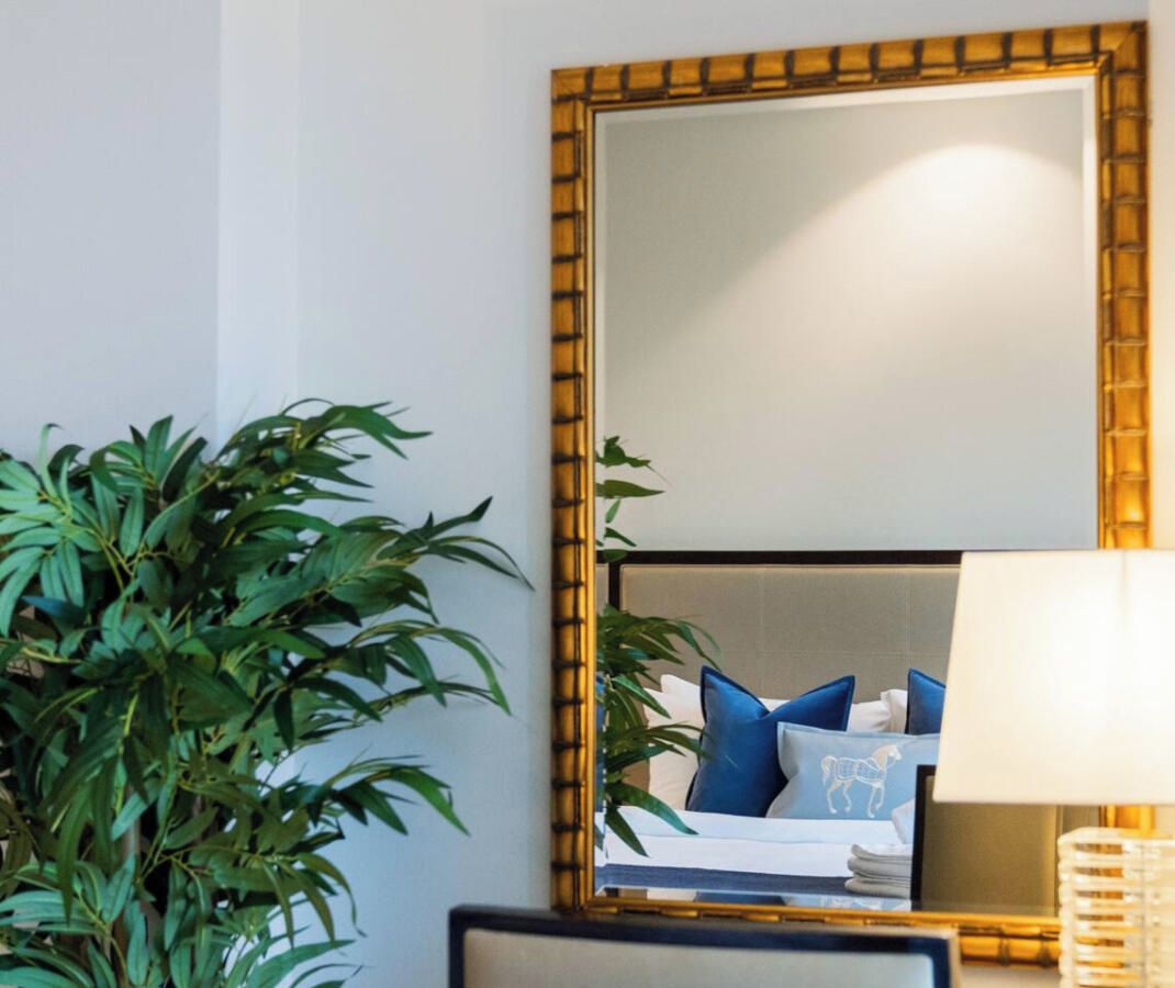 Une chambre d’hôtel avec un grand miroir, un lit avec des oreillers bleus et une plante en pot.