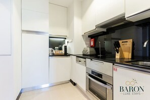 A modern kitchen with white cabinetry, stainless steel appliances, and a black countertop. - The Classic • JW Marriott (Dubai)