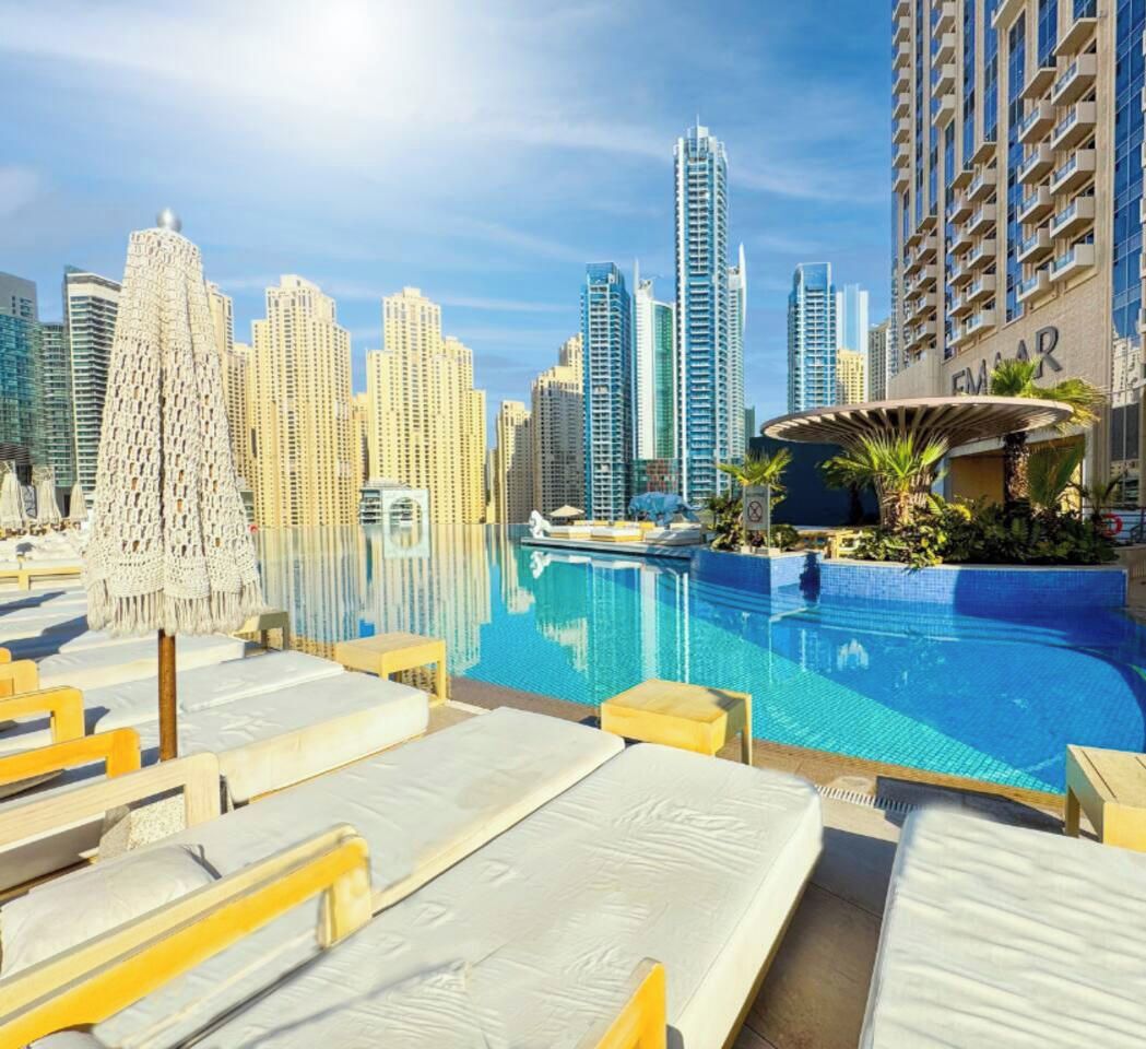 A pool area with lounge chairs, a water feature, and a city skyline in the background.