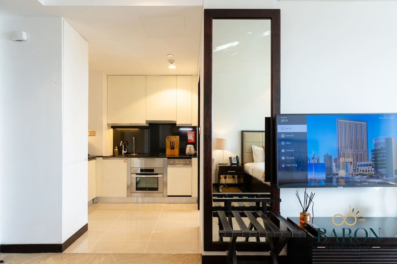 Una habitación de hotel moderna con kitchenette, una cama y un televisor que muestra un paisaje urbano.