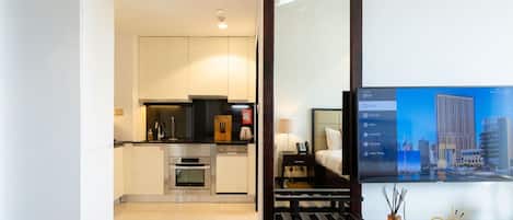 Une chambre d’hôtel moderne équipée d’une kitchenette, d’un lit et d’un téléviseur diffusant des images d’un paysage urbain.