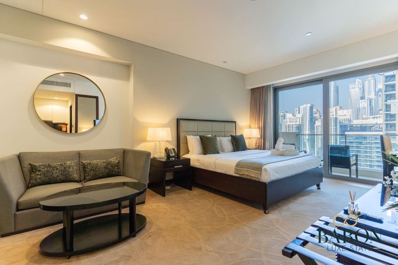 Een hotelkamer met een bed, een slaapbank, een ronde spiegel, een nachtkastje en uitzicht op de stad.