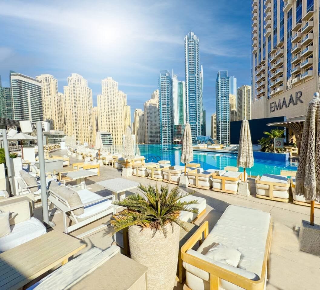 A rooftop pool area with lounge chairs and umbrellas, surrounded by high-rise buildings.