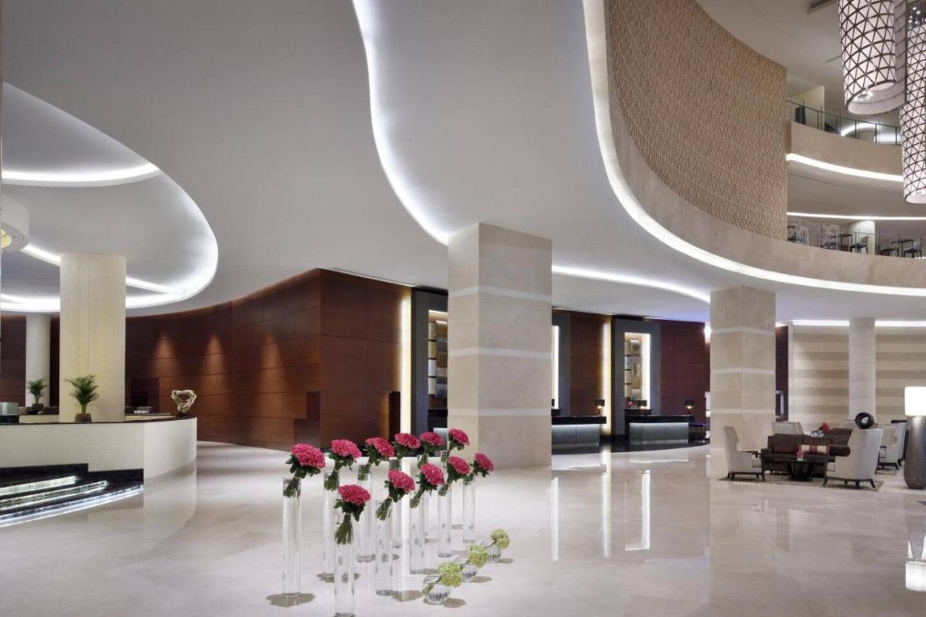 Un hall d’entrée moderne doté d’un plafond incurvé, d’un comptoir de réception et d’un espace détente avec des tables et des chaises.