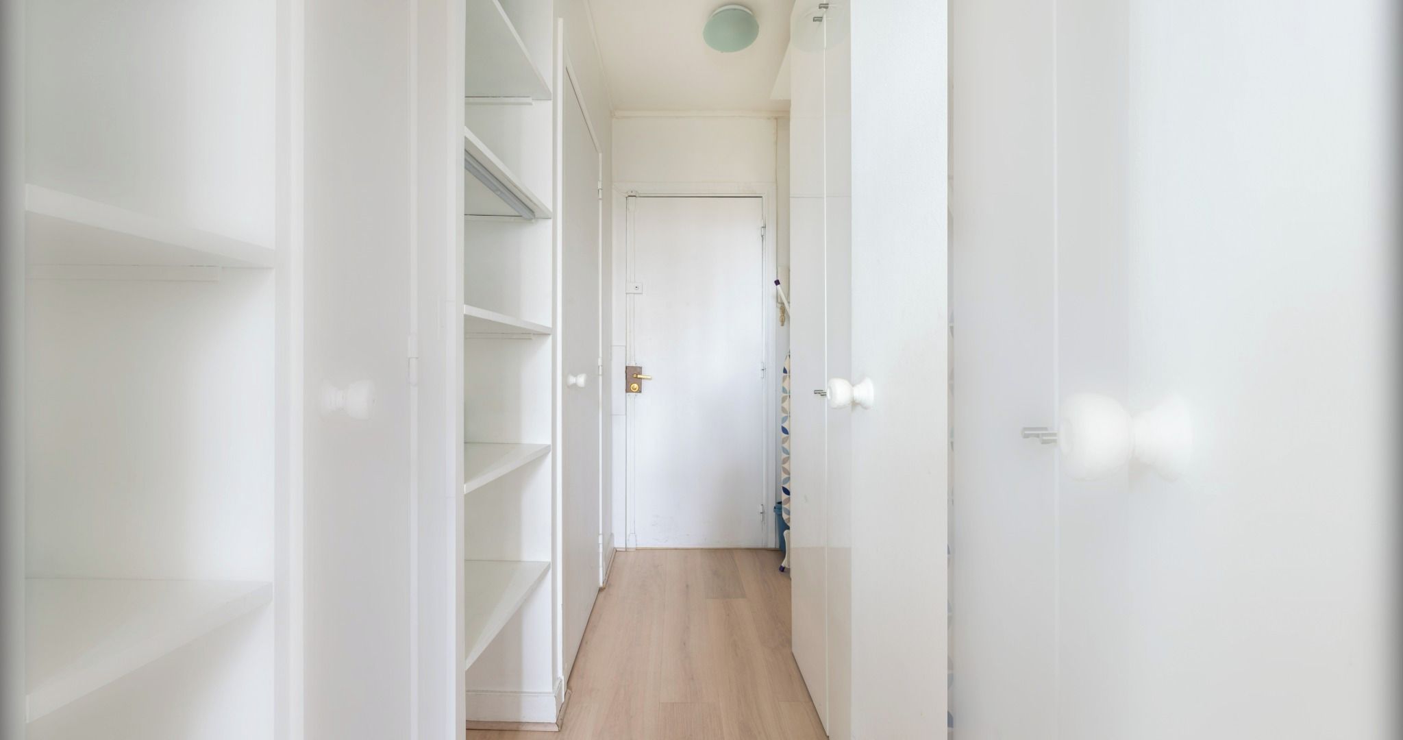 A narrow hallway with white walls and wooden flooring leading to a door at the end.