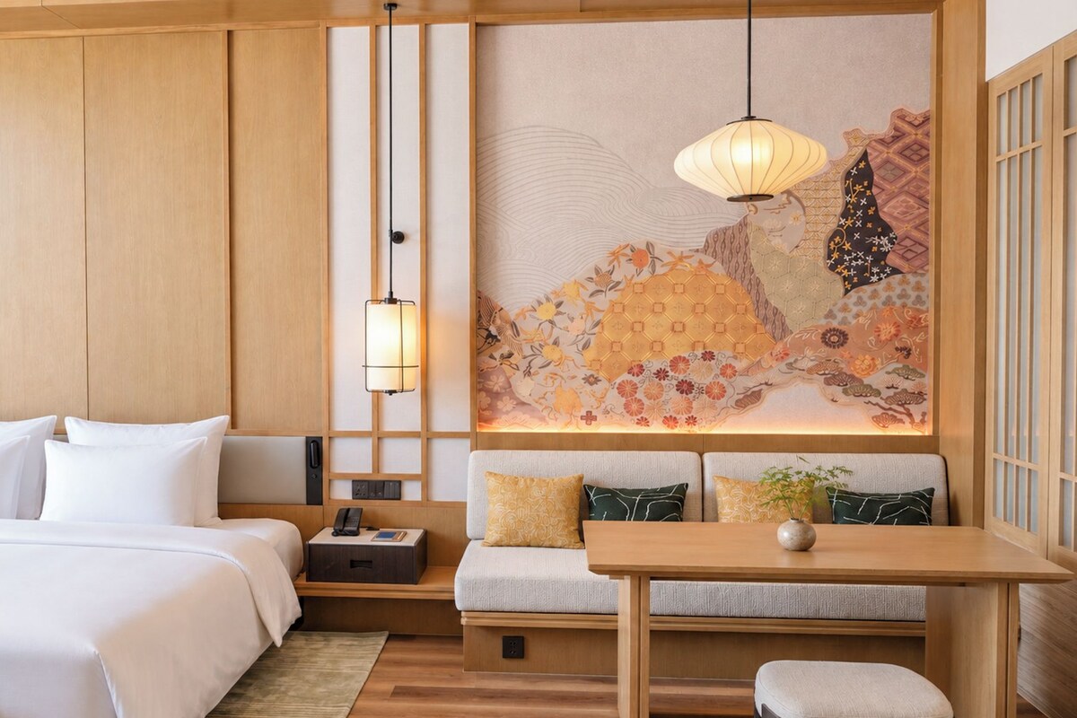 A hotel room with a bed, bedside table, lamp, and a decorative wall.