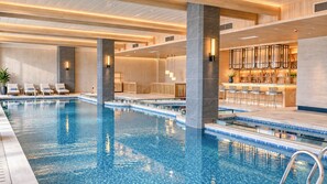 Une grande piscine intérieure dotée de plusieurs couloirs de nage, de chaises longues et d’un espace bar.