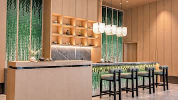 A modern bar area with a marble countertop, bar stools, and a green patterned wall.