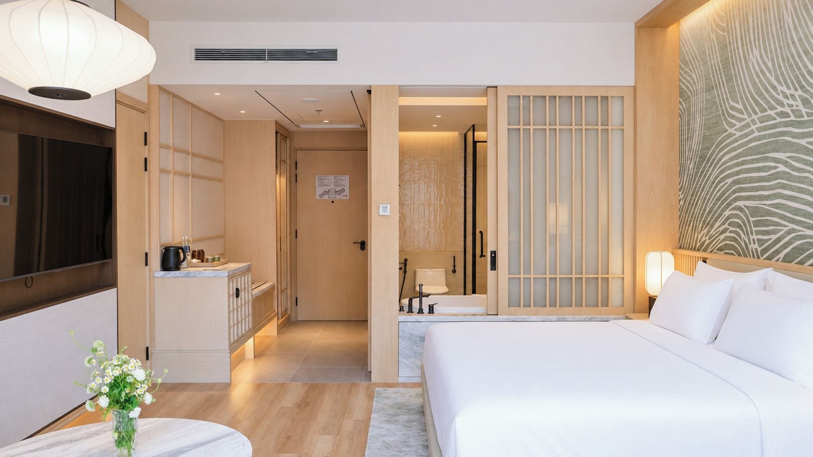 A hotel room with a bed, bedside table, and a view of the bathroom.