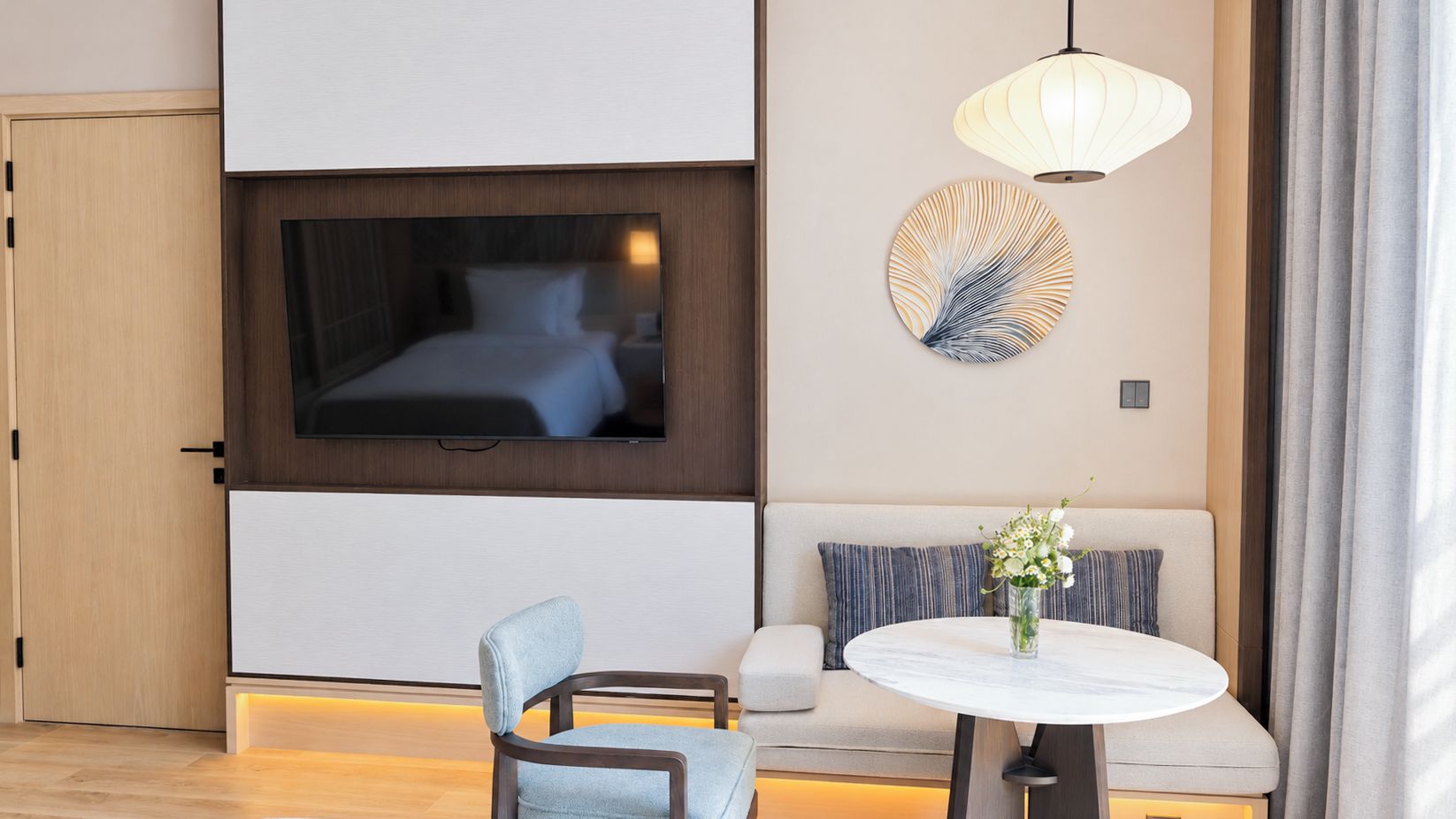 A hotel room with a bed, a television, a sofa, a round table, and a wall-mounted lamp.