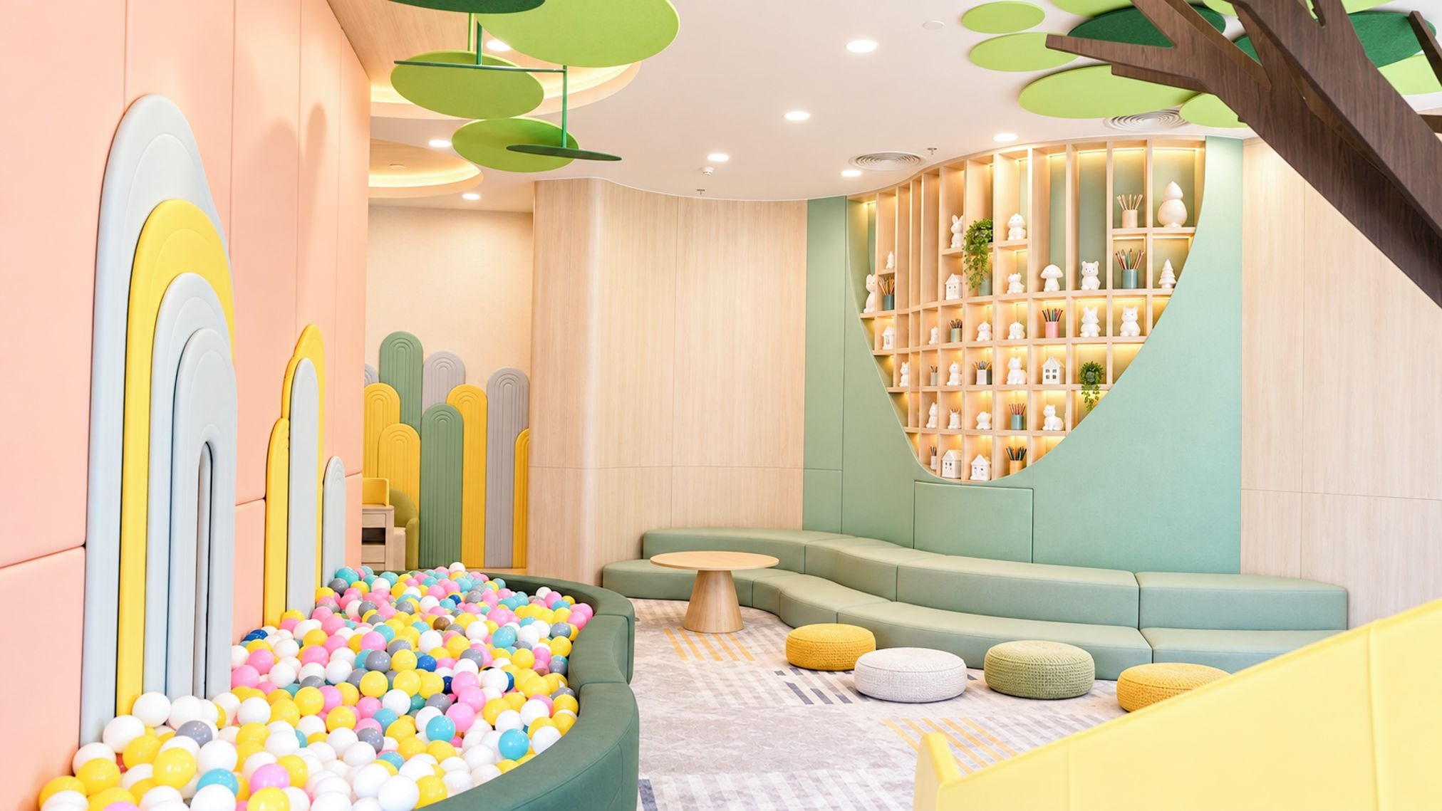 A children's play area with a ball pit, cushioned seating, and a wall with shelves.