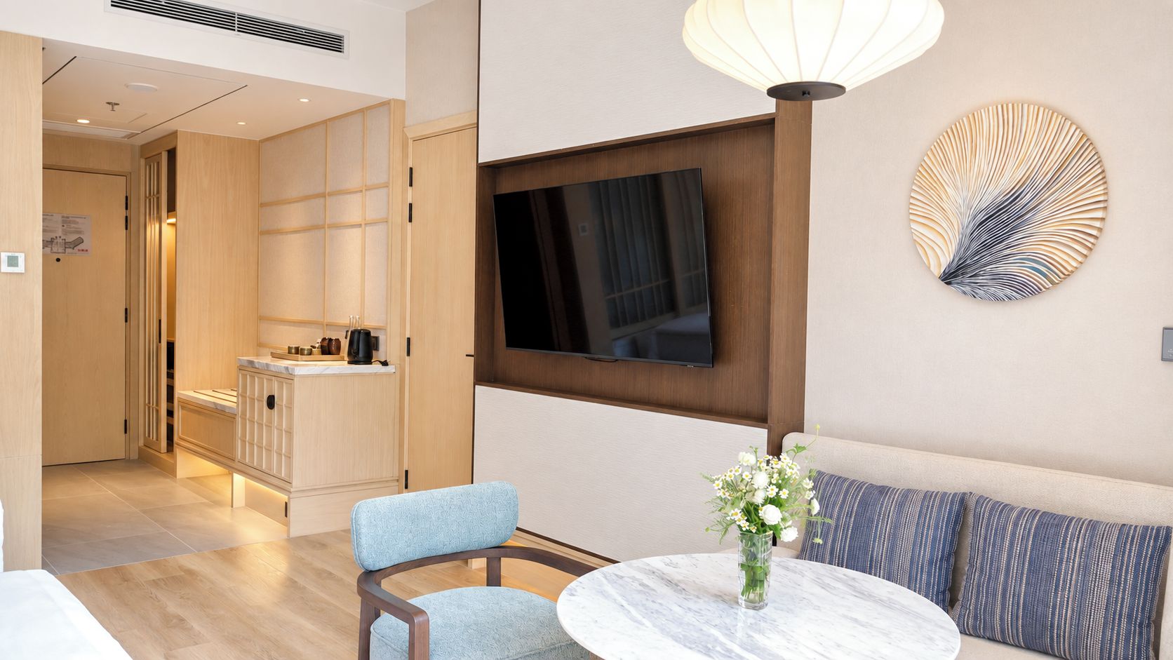 Ein modernes Hotelzimmer mit Essbereich, einer Couch, einem an der Wand befestigten Fernseher und einem Wandkunstwerk.