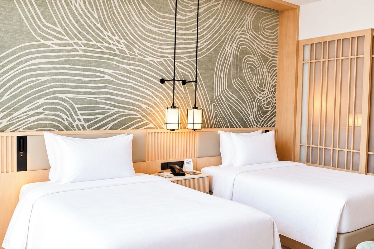 A hotel room with two beds, a wooden headboard, a wall with a wavy pattern, and a sliding door with a grid design.