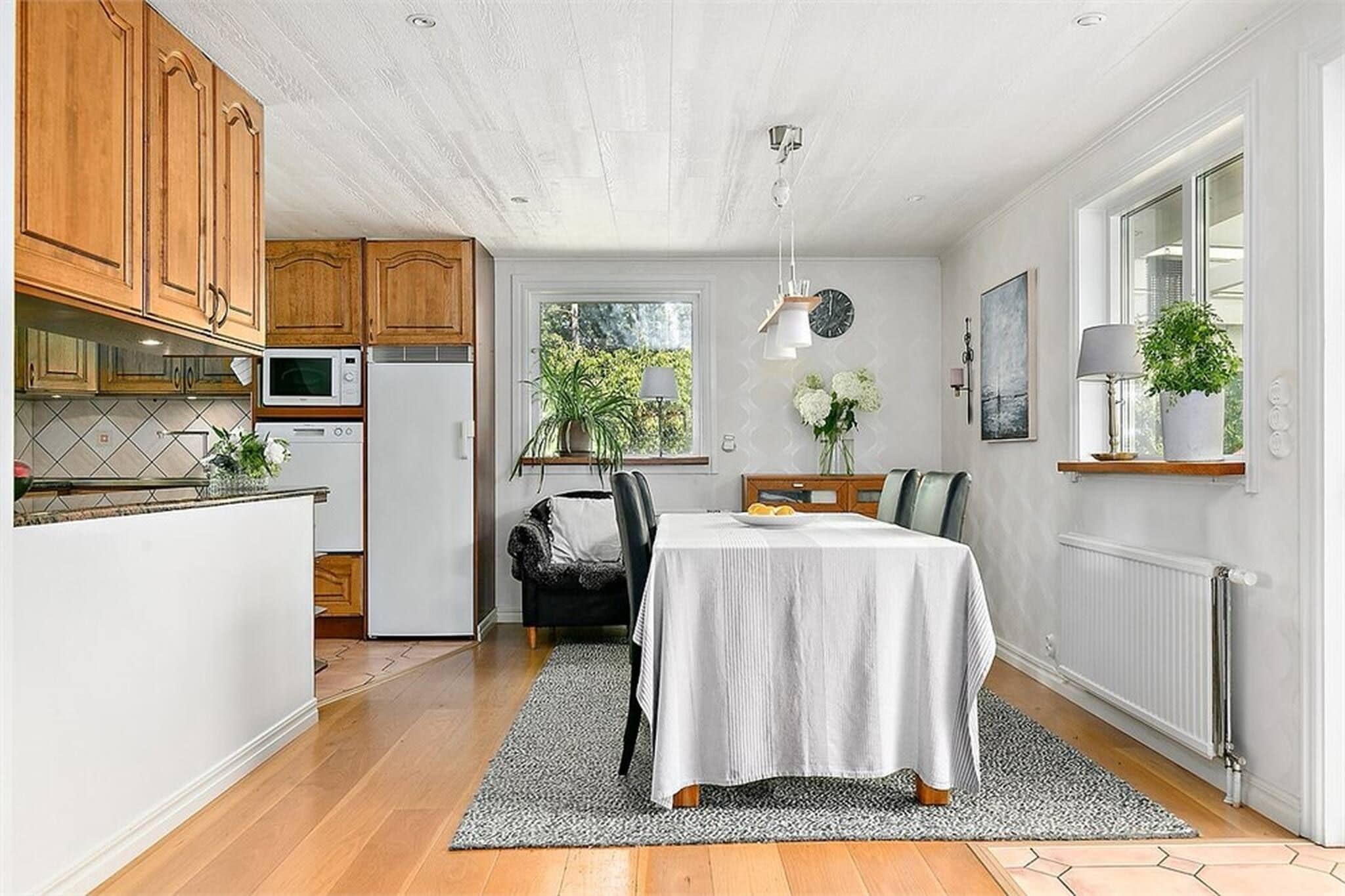 A compact kitchen with wooden cabinets, a dining table with a white tablecloth, and a black chair.