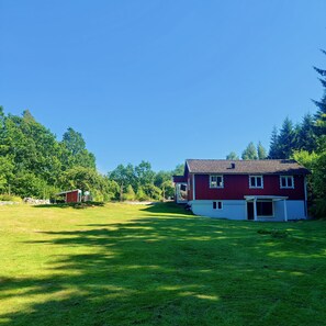 A red house with a white porch and a small shed in a grassy yard.