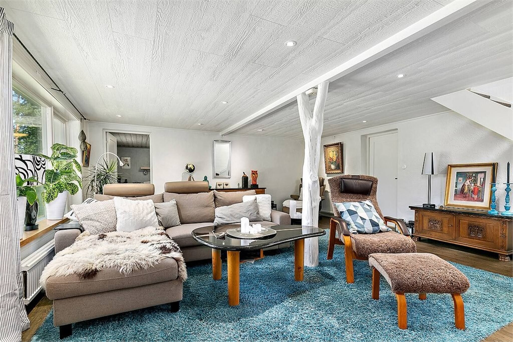 A spacious living room with a high ceiling, a large window, and a blue carpet.