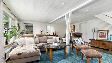 A spacious living room with a high ceiling, a large window, and a blue carpet.