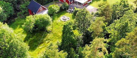 A red house with a large deck and a smaller red shed in a forested area.