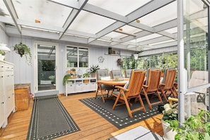 Um solário com piso de madeira, uma mesa de jantar com cadeiras e plantas em vasos.