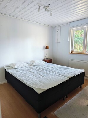 A bedroom with a large bed, a bedside lamp, a window with a view, and a ceiling light fixture. - Hazelnut Villa - Lake & Town Retreat (Osby)