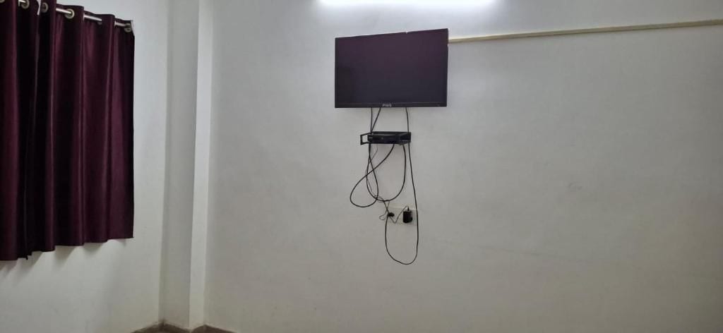 Una habitación con un televisor de pantalla plana montado en la pared, una regleta de enchufes y una cortina a la izquierda.