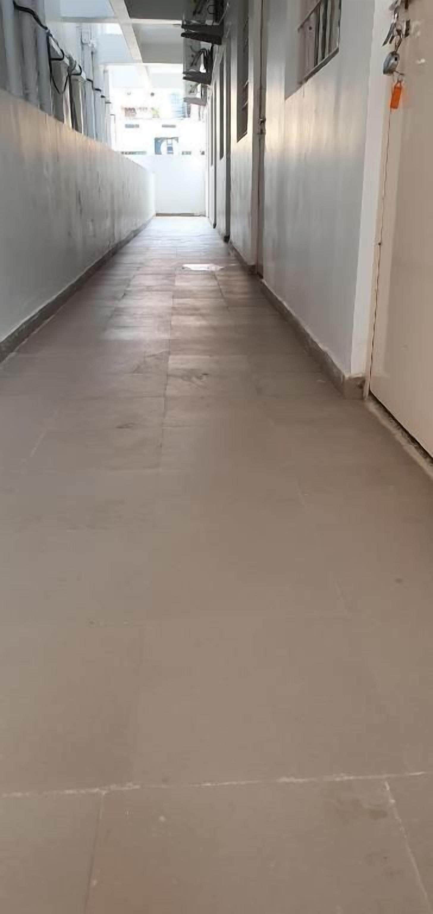 Un largo y estrecho pasillo con suelo de baldosas que conduce a una puerta al final.