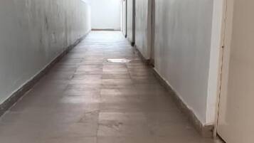 Un largo y estrecho pasillo con suelo de baldosas que conduce a una puerta al final.
