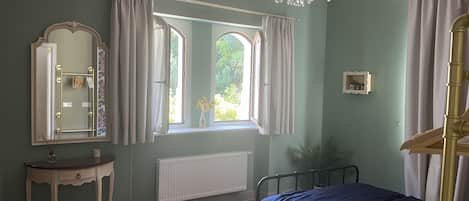 A bedroom with a bed, a vanity with a mirror, a radiator, and a window with curtains.