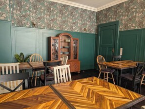 Un comedor con una mesa de madera en patrón espiga, paredes revestidas de verde y un clásico mueble de madera.