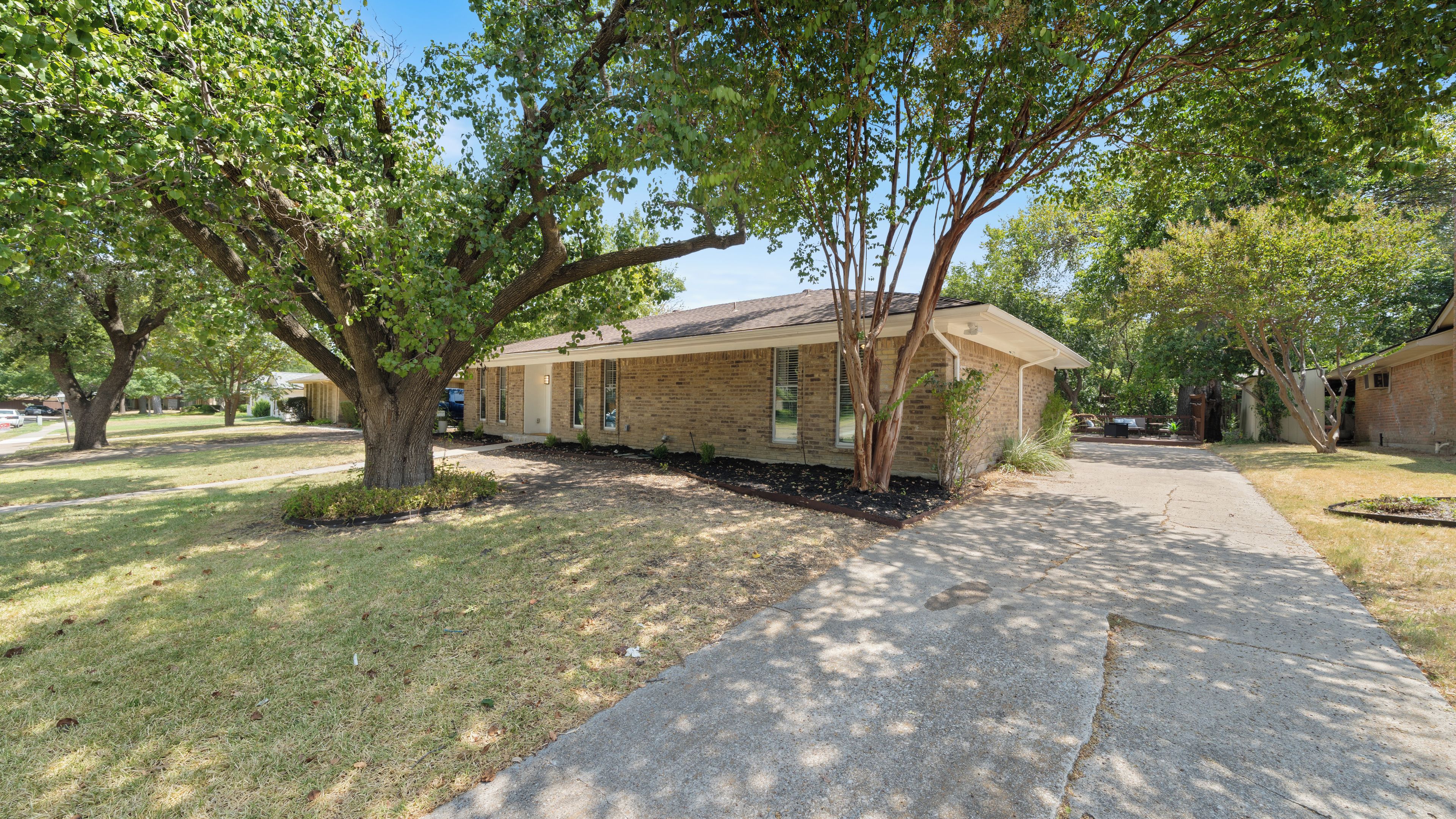 A residential property with a brick house, a driveway, and surrounding trees.
