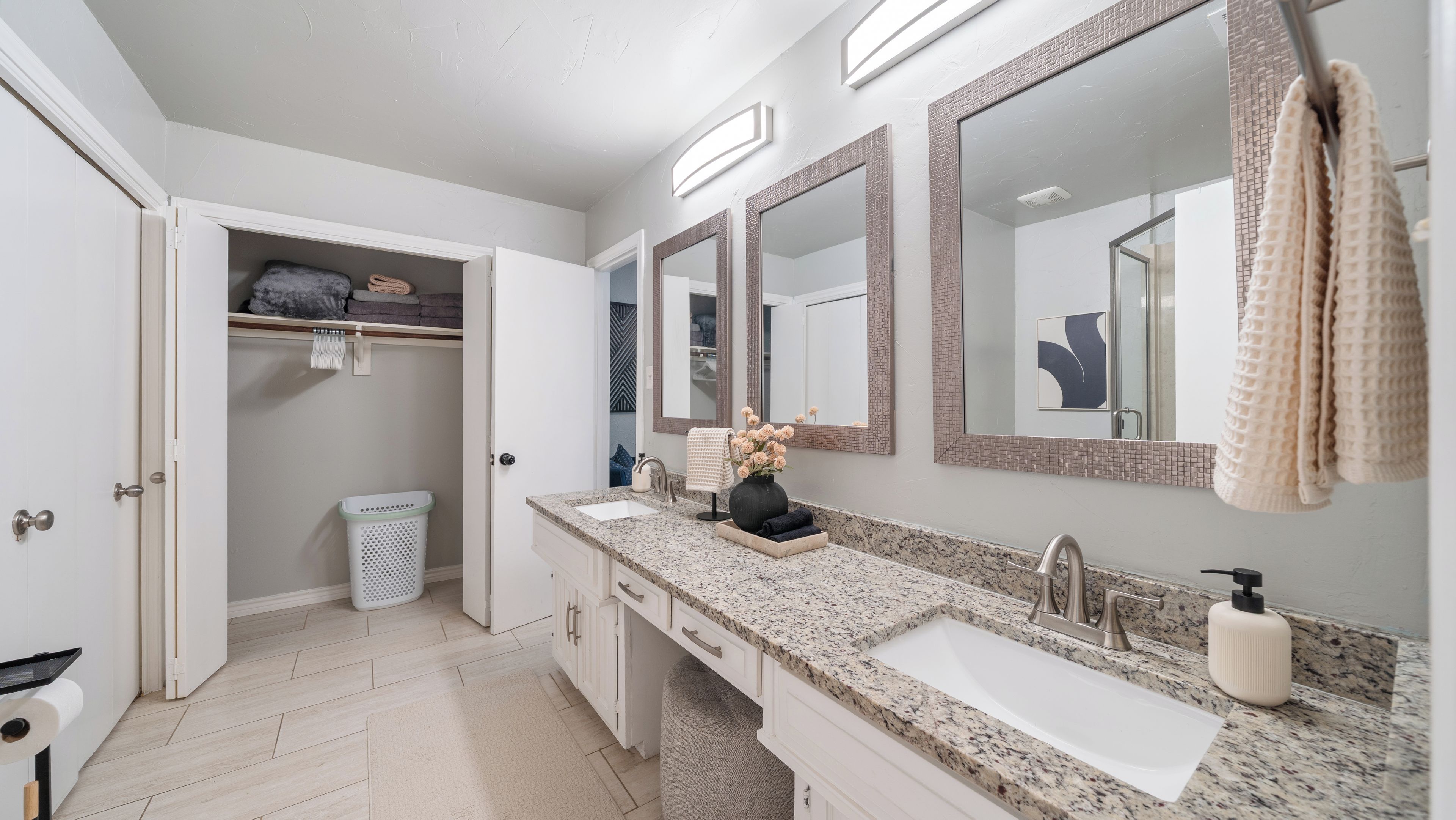 A bathroom with a double sink, a mirror, a towel rack, and a laundry basket.