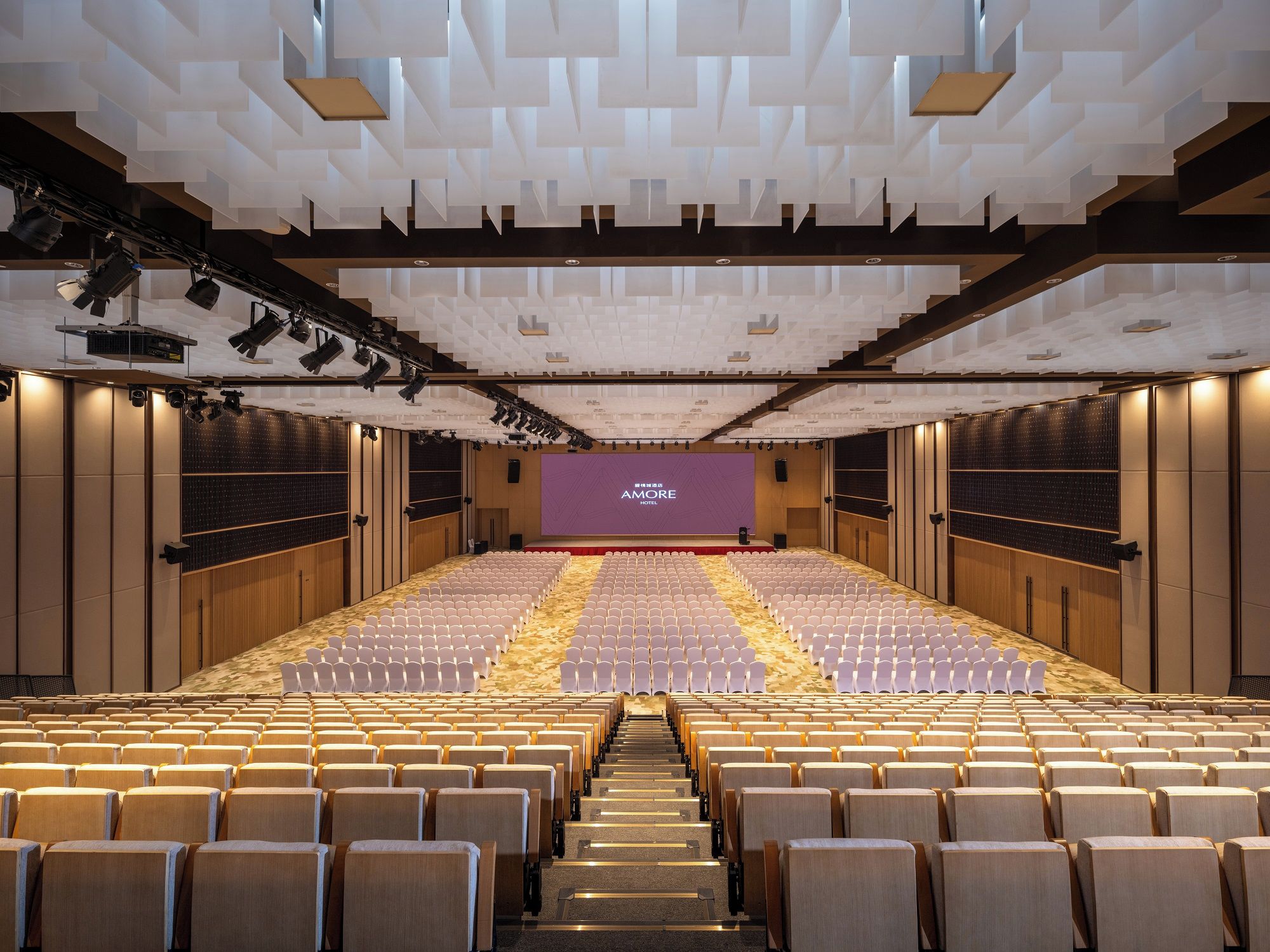 A large auditorium with rows of seats, a stage, and a modern ceiling design.