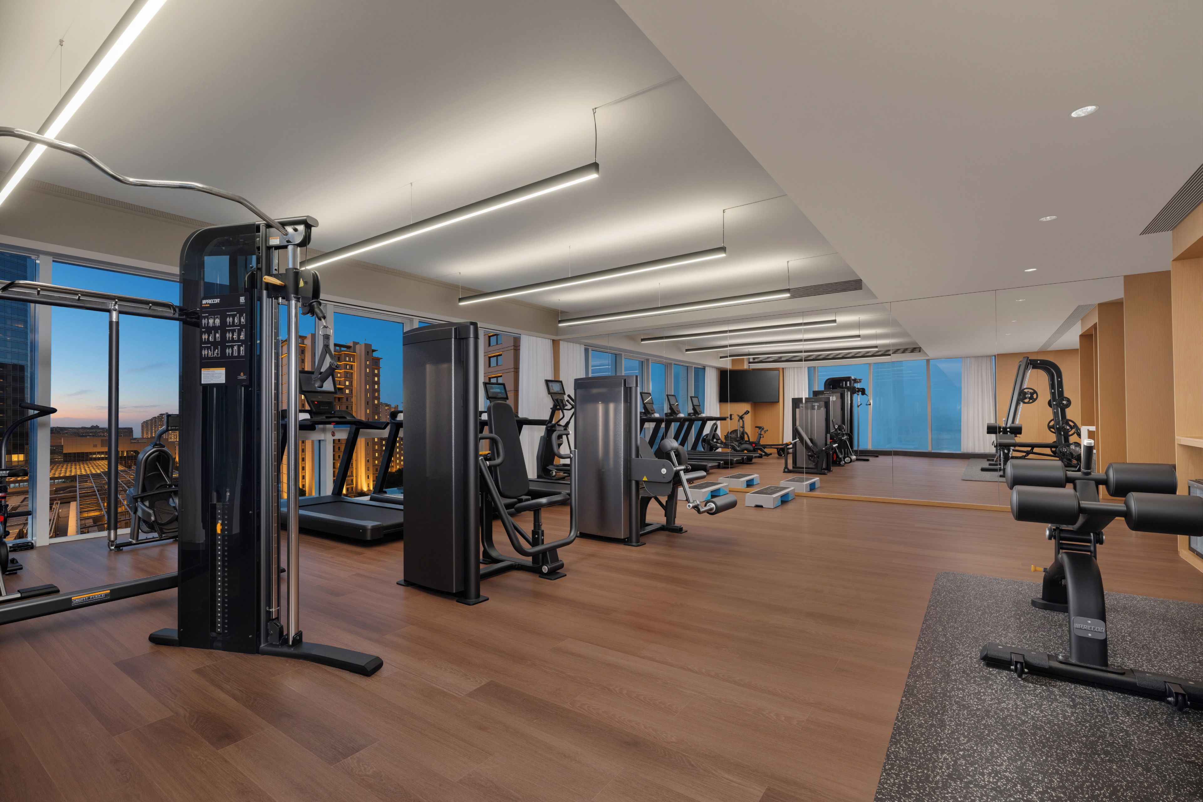 A modern gym with various exercise equipment, large windows, and a city view.