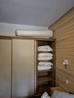 A bedroom with a wooden wardrobe, a bed with a patterned pillow, and a wall socket. - Länsirinne F 24 | 2BR Apt in Ruka Centre (Kuusamo)