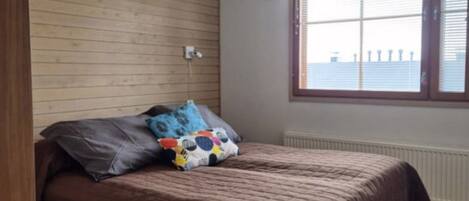 Una camera da letto con una testiera in legno, un letto con copripiumino marrone, una finestra con vista e una tenda a motivi.
