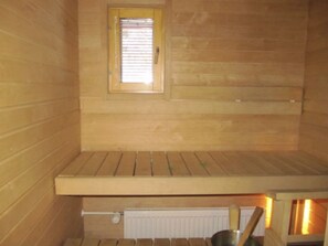 A sauna room with wooden walls, a bench, a small window, and a radiator. - Länsirinne F 24 | 2BR Apt in Ruka Centre (Kuusamo)