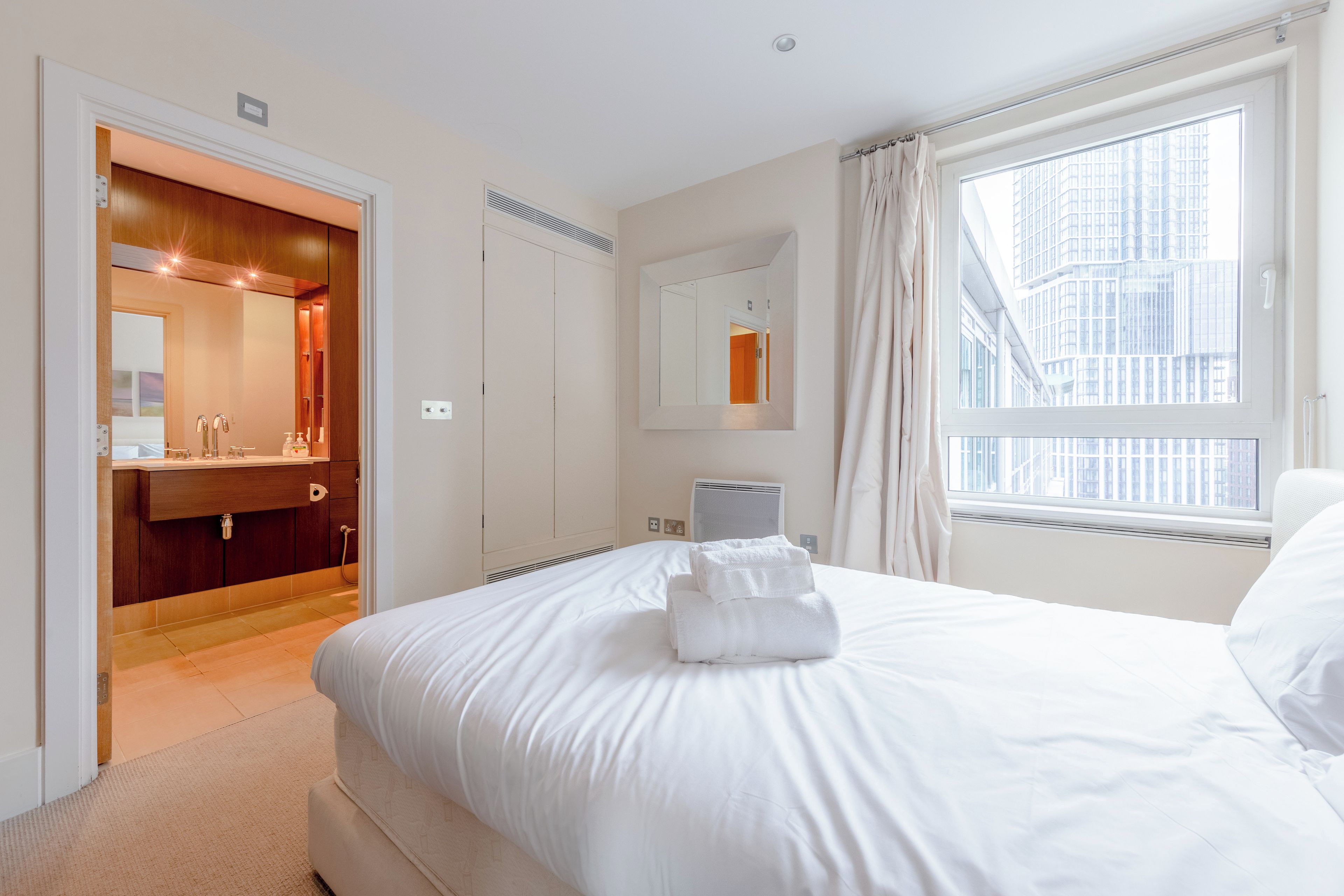 Habitación de hotel con cama, baño con espejo y ventana con vista a la ciudad.