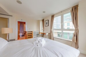 A hotel room with a bed, a desk, a chair, a radiator, and a window with curtains. - Sleek 3BD flat with Stunning City Views, Vauxhall (London)