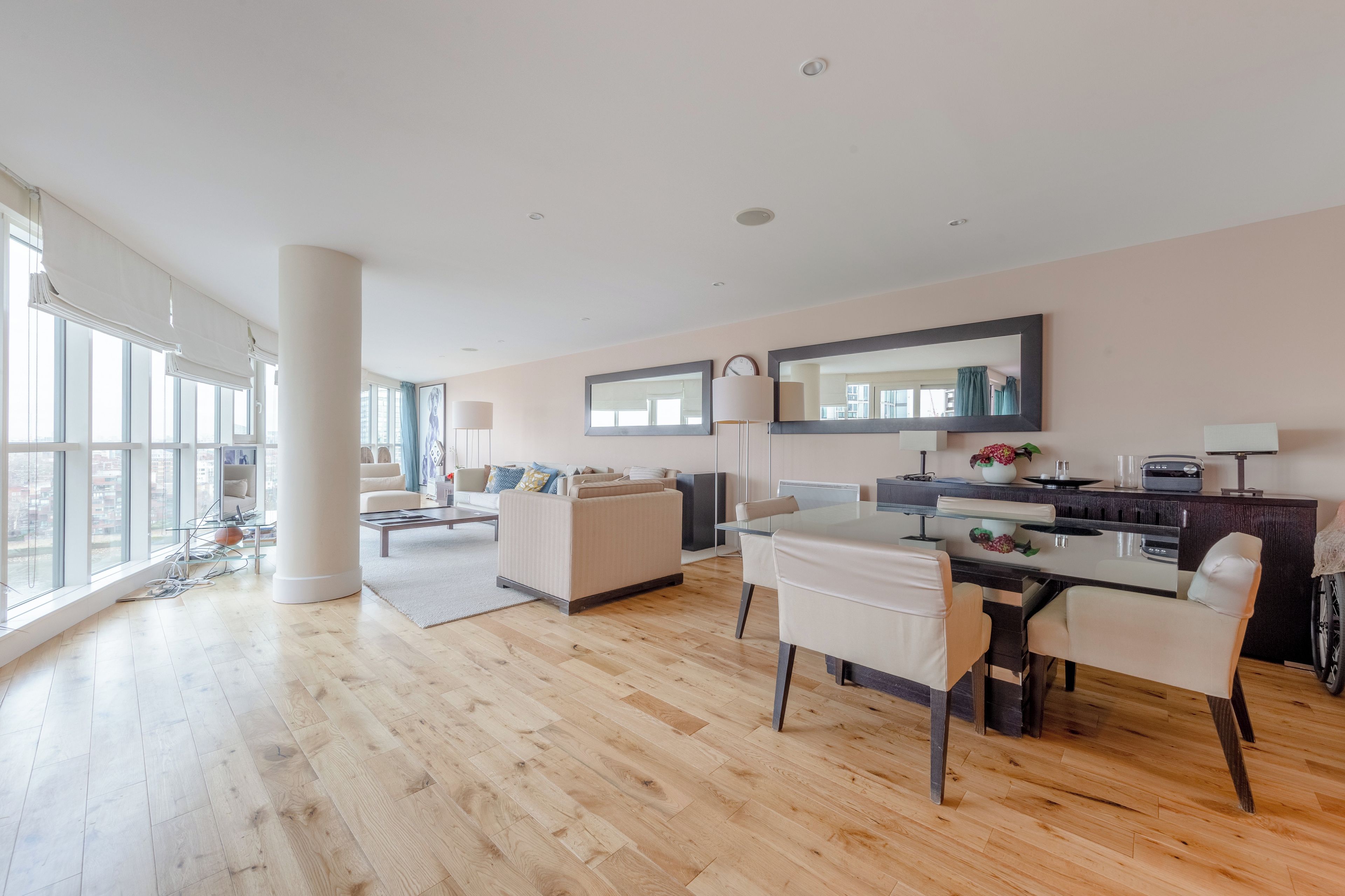 A spacious living area with a large window, a dining table, and a kitchen area.