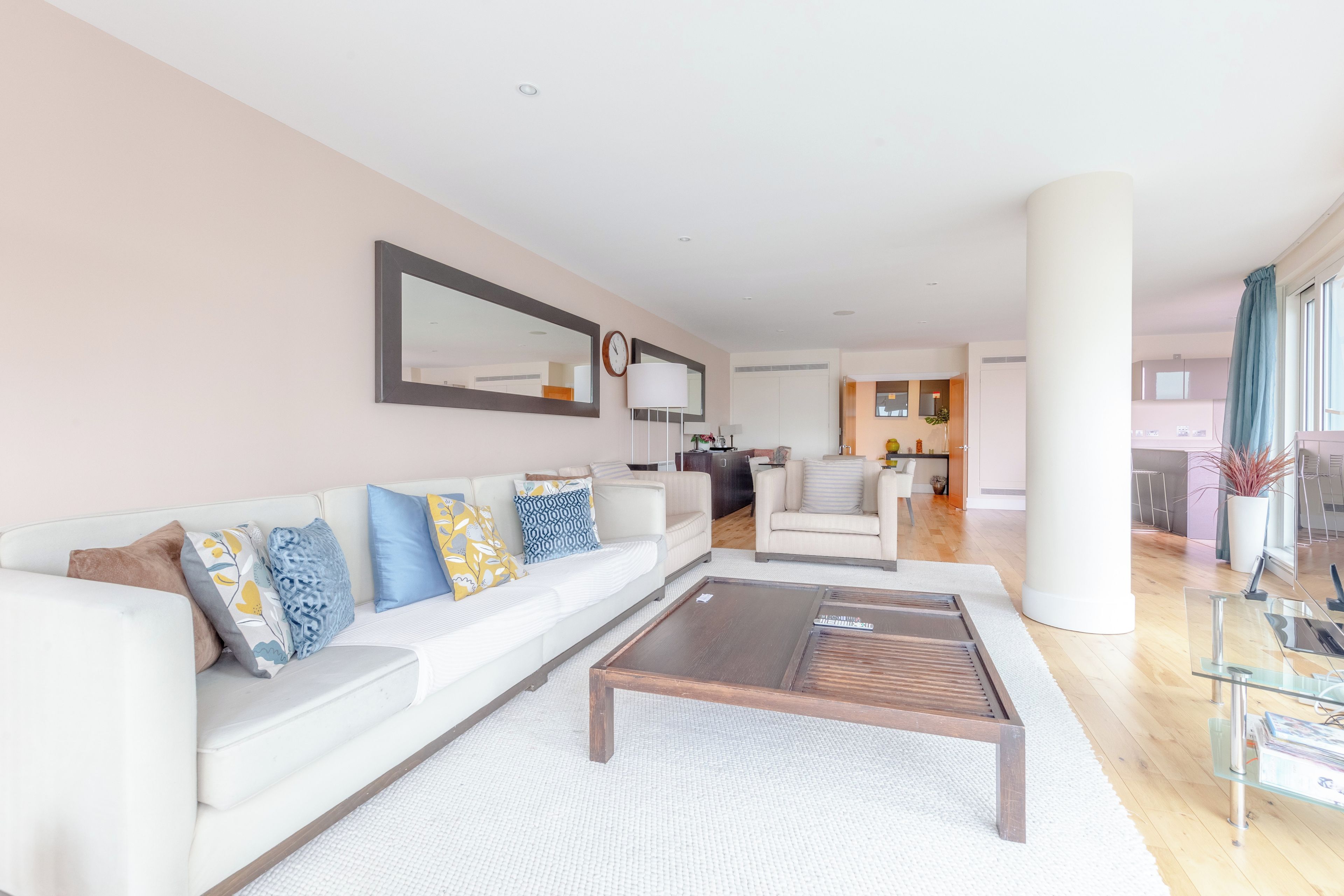 A modern living room with a white sofa, a coffee table, and a large mirror.