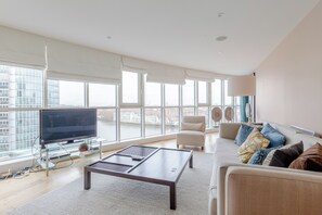 A modern living room with a large TV, comfortable seating, and a view of the city. - Sleek 3BD flat with Stunning City Views, Vauxhall (London)